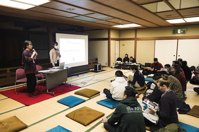 Attendees seated on cushions in a traditional tatami room during a presentation.