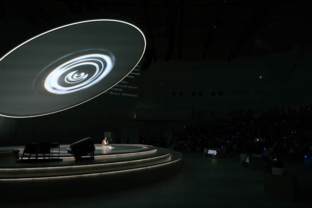 Dark auditorium stage with circular projection and seated audience