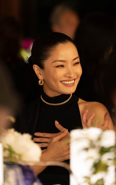 Smiling woman in black dress and gold jewelry at an event table