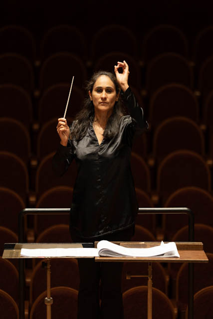 Female conductor standing at a podium holding a baton in an empty concert hall