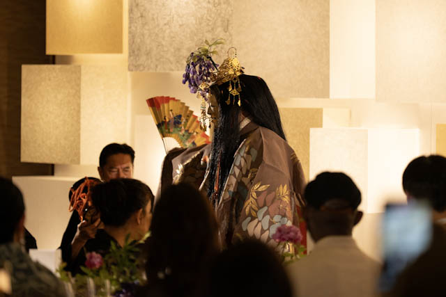 Performer wearing traditional Japanese costume and golden headdress holding fan